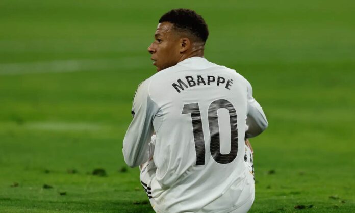 Kylian Mbappé sentado en el suelo durante un partido. 